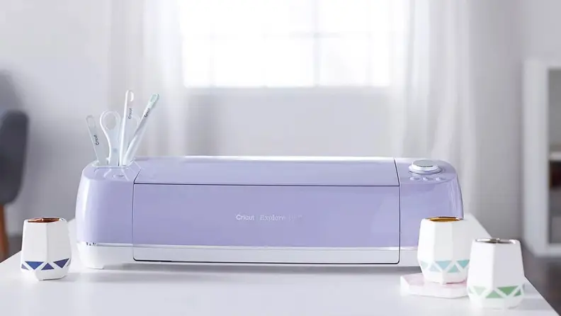 A purple Cricut machine sitting on a white desk in a sunny room.