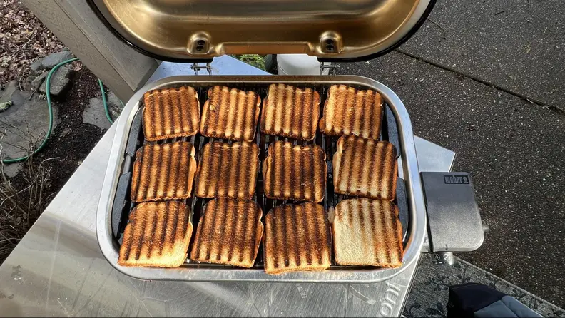 Slices of bread with grill marks cover the cooking surface, showing the even heating of the Weber Lumin.