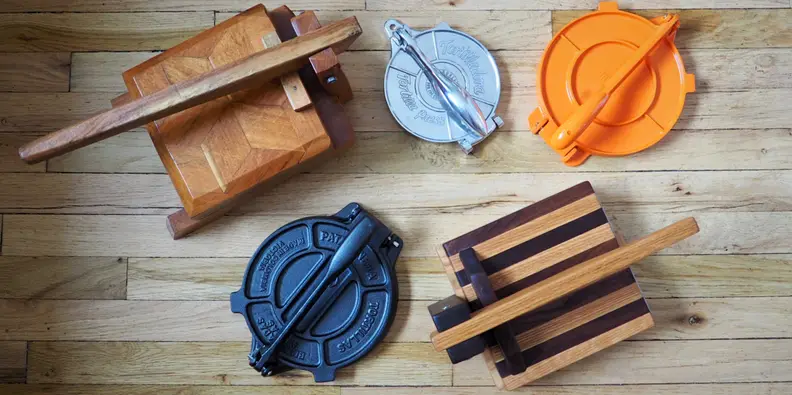 Five tortilla presses laid out on a wooden backdrop, shot from above.
