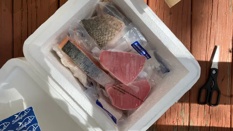 In a styrofoam box, there are frozen fish steaks, shrimp, and scallops.