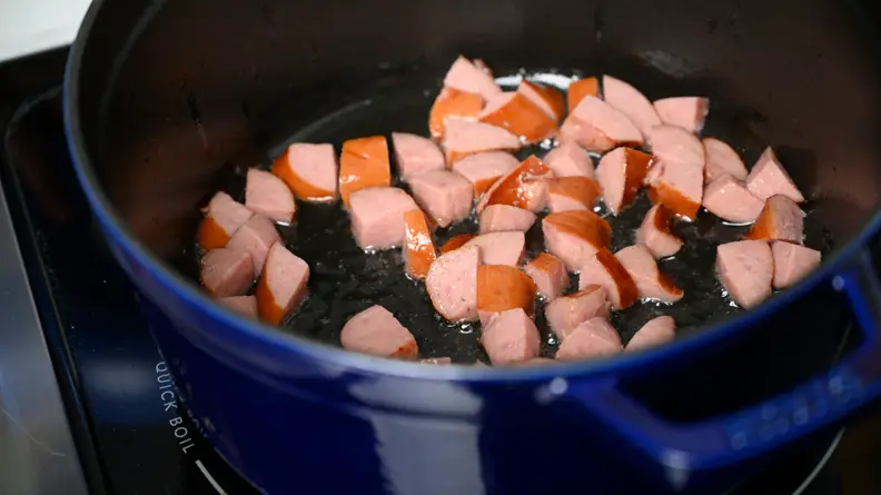 A pot with andouille sausage being sauteed in oil.
