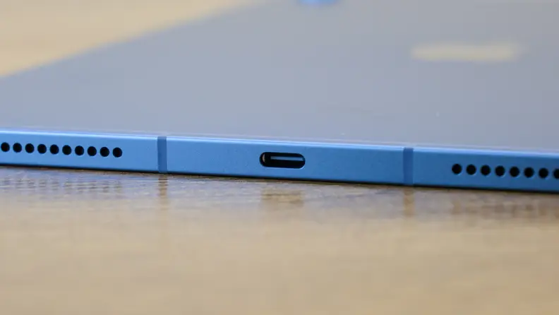 The blue Apple iPad 10 sits on a wooden desk with its thin profile and ports showing