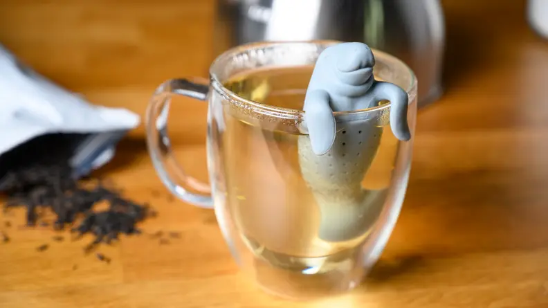 A tea infuser in the shape of a manatee hangs on the lip of a mug