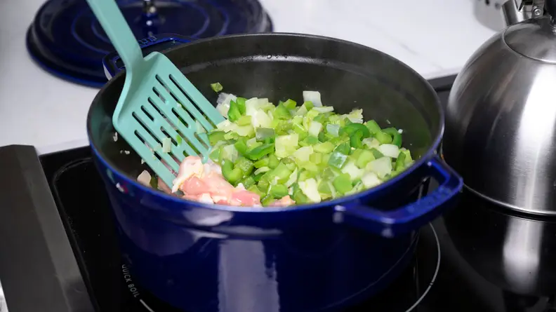 Raw chicken being stirred into a pot of fresh produce.