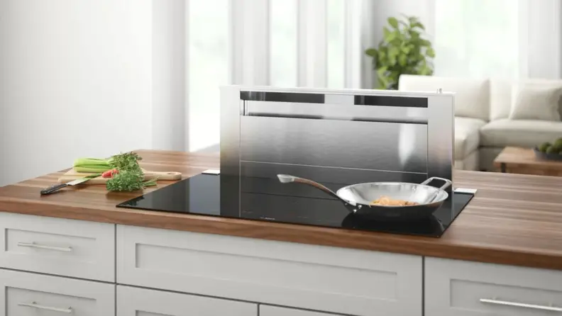 Bosch Benchmark Series induction cooktop in use in a kitchen with a stainless-steel downdraft vent behind it.