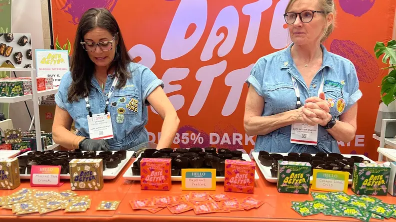 Two people in front of a Date Better Expo West display