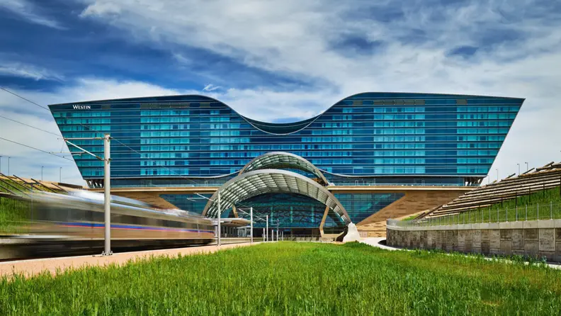 Exterior view of the Westin Denver International Airport hotel with its curved glass architecture and a train passing in the foreground.