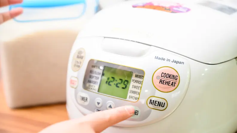 Hand pressing a button on a Zojirushi rice cooker.