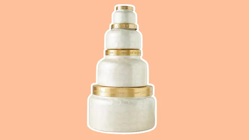 A stack of four Capri Blue candle jars in ascending order of sizes on an orange background.