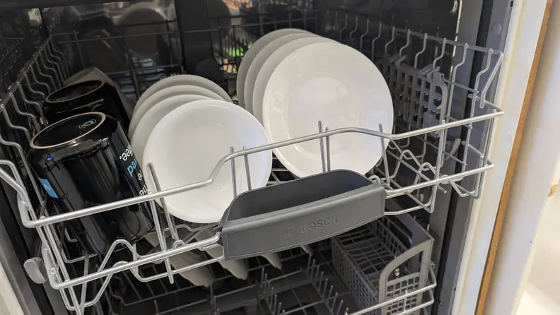 A close-up of the Bosch 100 Series SHE3AEM2N dishwasher's upper rack, which is full of spotless bowls and mugs.