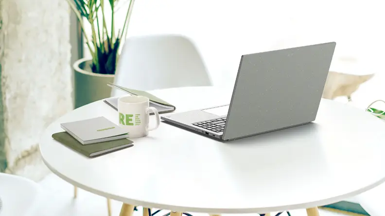A light gray Acer Aspire Vero 16 sits on a white tabletop next to a coffee and notebooks.