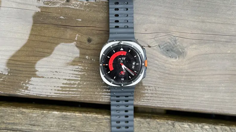 A Samsung Galaxy Watch Ultra laying on a wet patio deck outdoors.