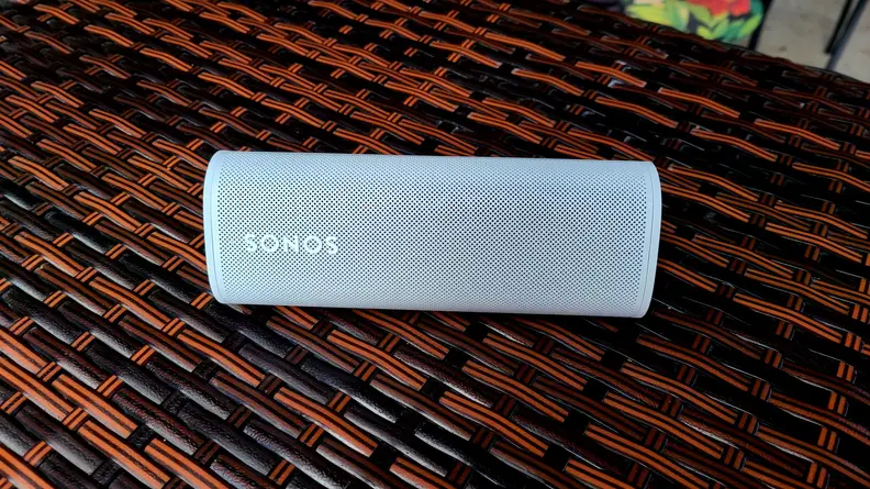 The white and tubular Sonos Roam is set atop a brown and black vinyl bar