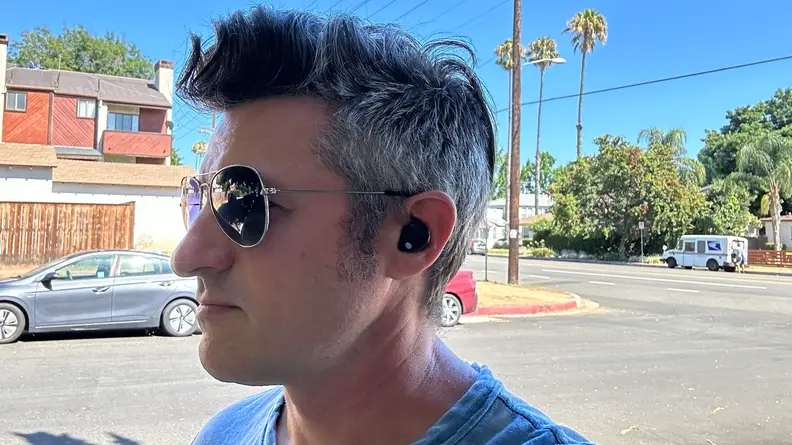 A man in sunglasses wearing the Sony WF-1000XM5 outside.
