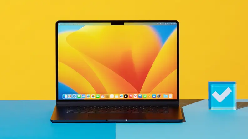 MacBook Air 15 M2 laptop computer in black color sitting on top of blue surface next to acrylic paperweight with screensaver display on screen.