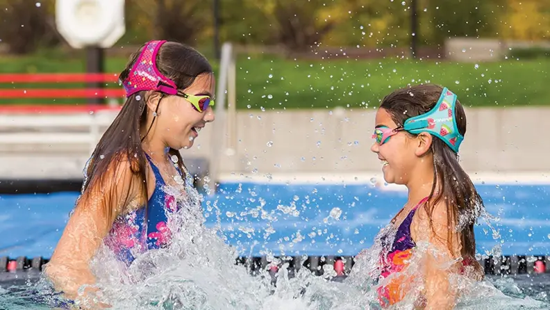 Two girls jump in the water wearing their Finis Frogglez kids swimming goggles