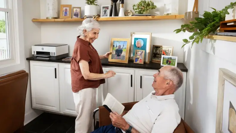 An older couple smiles together in a bright home office featuring an HP Smart Tank 6001 on the back counter.
