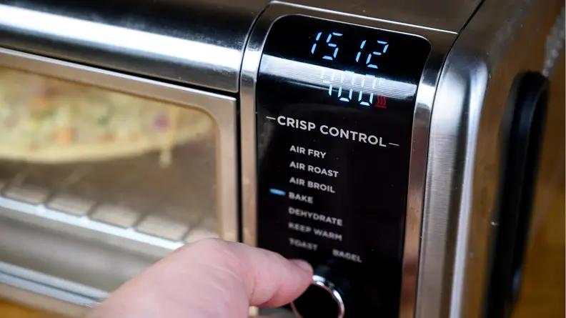 A person turns the dial on the Ninja Foodi Air Fryer Oven while setting the temperature and time.