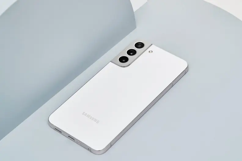 A white Galaxy S22+ lying against a grey background.
