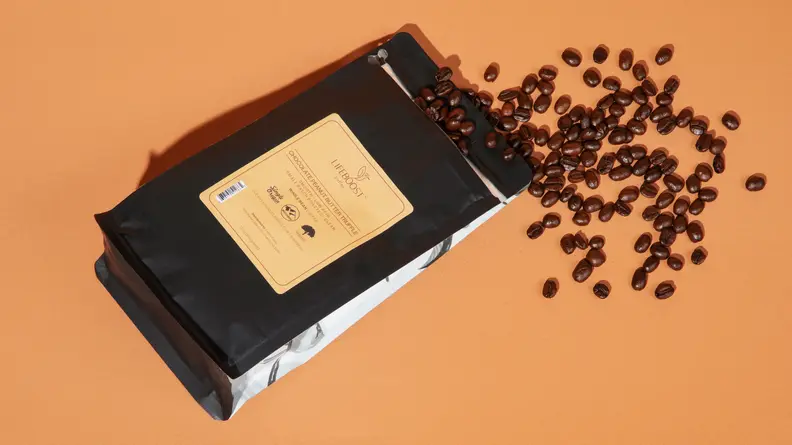 A bag of Lifeboost Coffee with coffee beans spilling out of the bag, with an orange background.