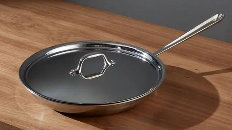 An All-Clad pan is photographed on a kitchen island with the lid on, its silver metal gleaming in the light.