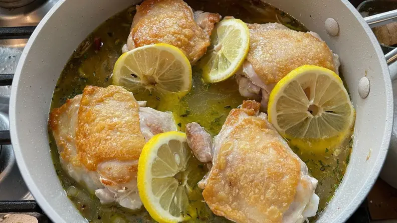 Browned chicken thighs prepared with slices of lime in one of the cookware's pans.
