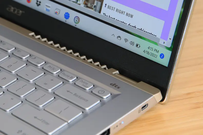 A close up of an open and powered on laptop sitting on a light brown wooden surface.