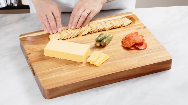 Hand arranging crackers in wooden cutting board well