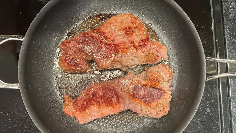 Two cuts of steak being seared on the Anolon X.