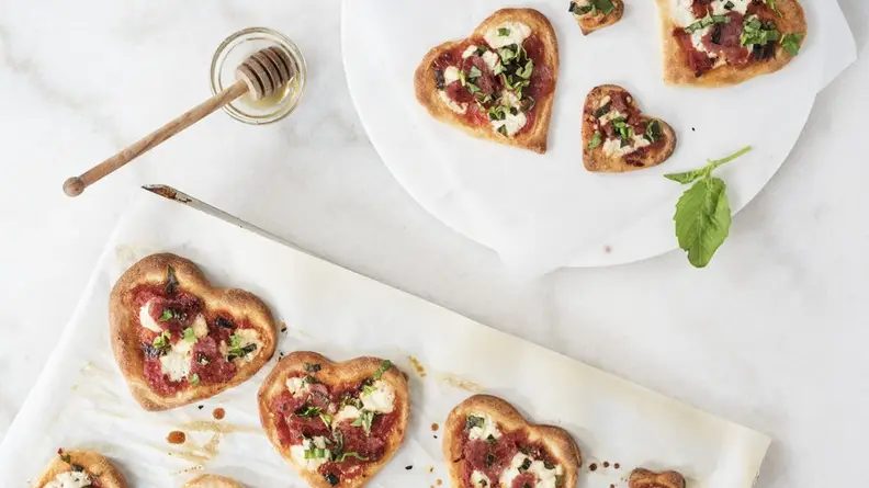 Several heart-shaped mini pizzas on parchment paper
