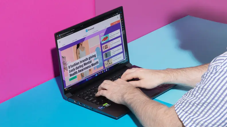 A person typing on the Acer Swift X 14 on a blue table with a pink background.