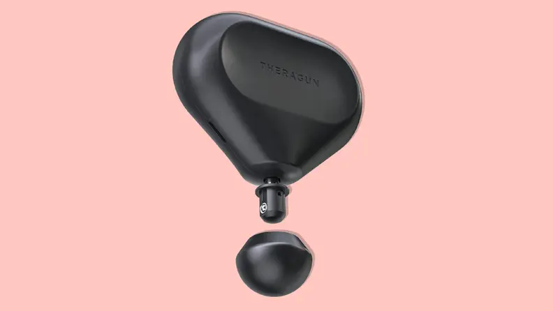 A black Therabody Theragun Mini massage gun on a pink background.