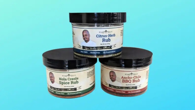 Three jars of chef-made spice blends on a blue background in the following flavors: Nola Creole Spice Rub, Citrus-Herb Rub, and Ancho-Chile BBQ Rub.
