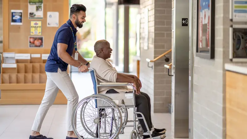 A man pushing a man that's sitting in a wheelchair.