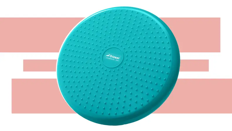 The disk-like Trideer Inflated Wobble Cushion in teal in front of a pink and white background.