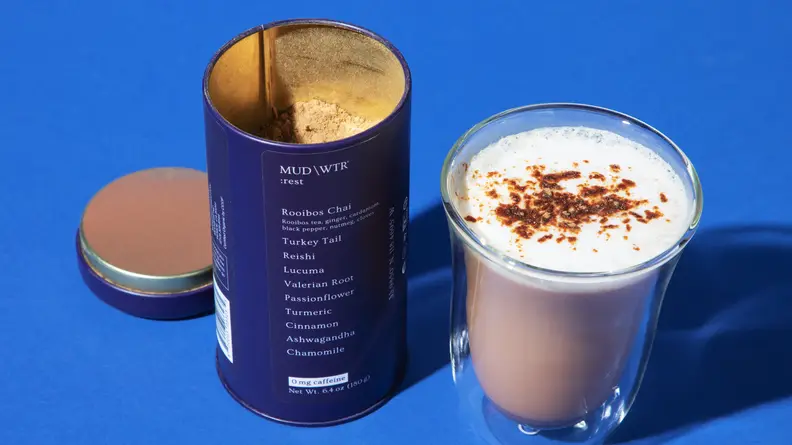 A clear mug of Mud/Wtr mixed with water and a blue Mud/Wtr container open next to it.