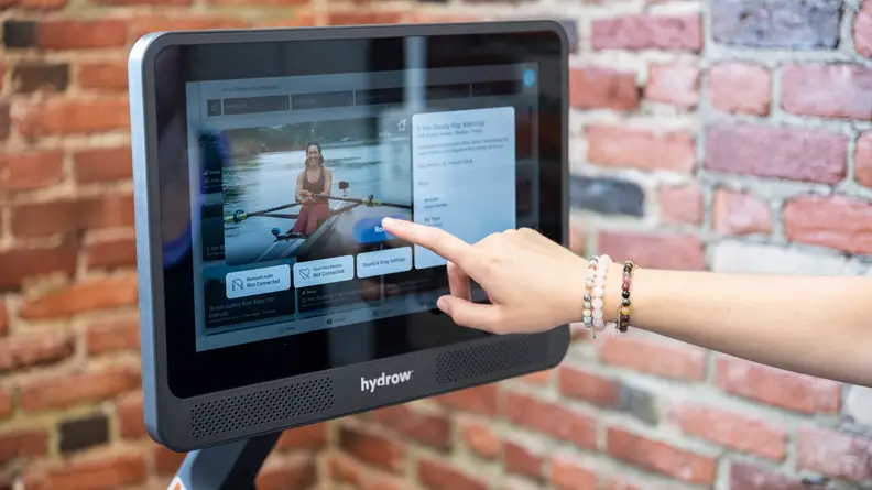 A person taps the Hydrow Wave touchscreen to select a workout.