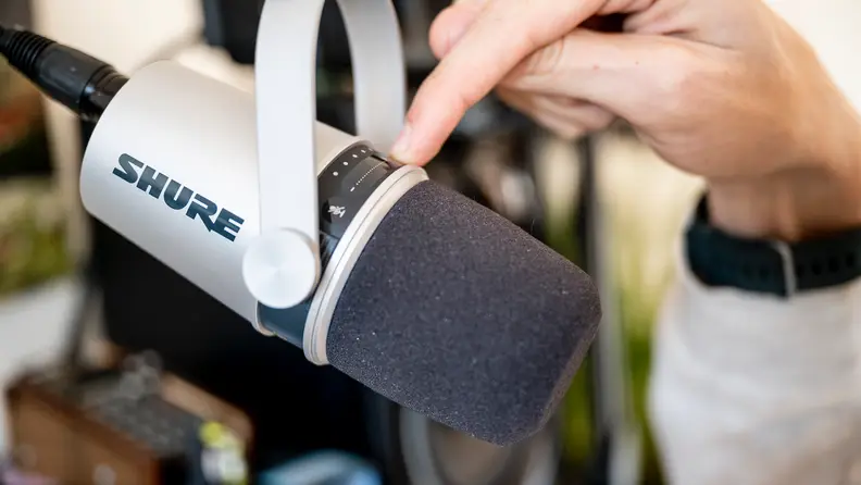 A person adjusts a white Shure MV7 USB microphone