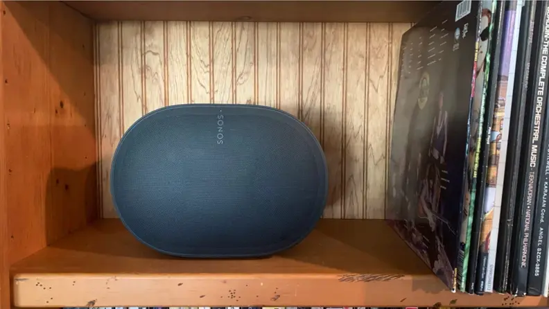 The Sonos Era 300 on a wooden bookshelf with records leaning next to it.