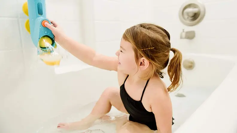 A little girl plays with a colorful bath toy in the shape of a submarine.