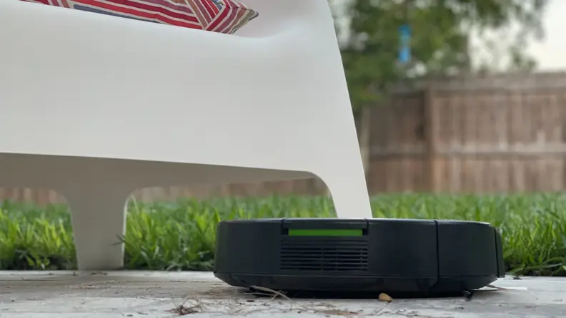 An iRobot vacuum on a patio with a chair in the background.