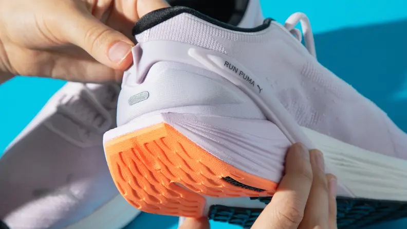 An orange rubber outsole heel on a pair of white running shoes.