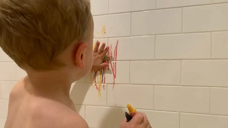 A small child scribbles on the wall with crayons.