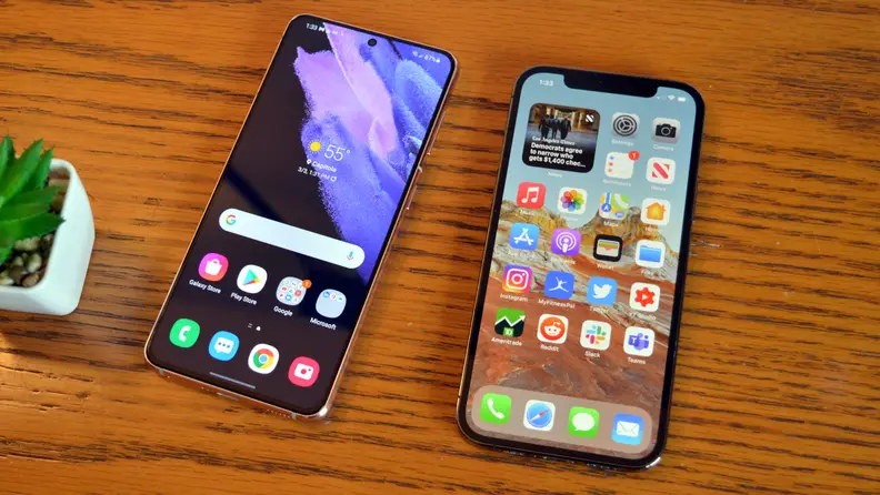 Two iPhones lying side by side on a brown table.