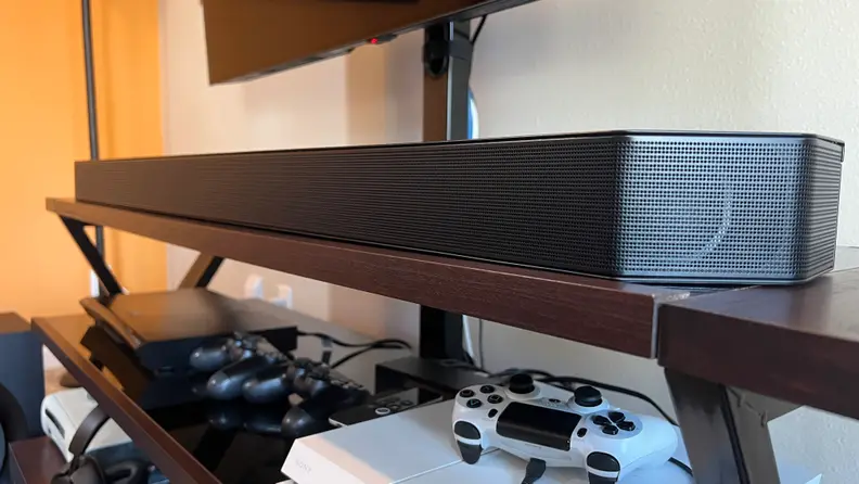 An angled shot of the Samsung HW-Q990B with Sony Playstation controllers on a shelf underneath it.