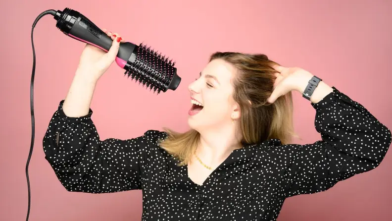 A woman "singing" into a Revlon One-Step Hair Dryer Brush as though it were a microphone