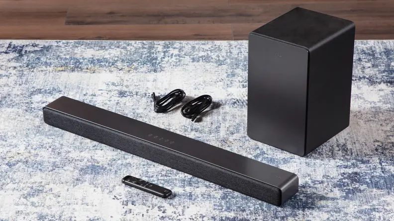 Black, rectangular TCL Q Series (Q6310) 3.1-Channel Soundbar sitting on top of carpet next to two power cords