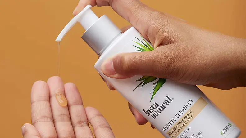 A person is holding out their hand palm side up and preparing to pump the InstaNatural Vitamin C Cleanser into it using their other hand.