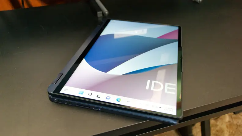 Navy blue Lenovo IdeaPad Flex 5i 14 folded in half into touchscreen tablet to hide keyboard on top of desk surface indoors.
