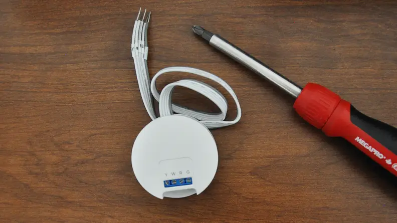 Interior piece of thermostat, cable, and screwdriver on wood tabletop.